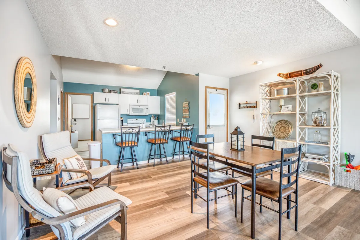 An inviting interior scene highlighting a dining table next to a kitchen bar area, with a nearby bookshelf. The setting is arranged for social gatherings, family meals, and casual conversation, reflecting a warm, communal atmosphere.