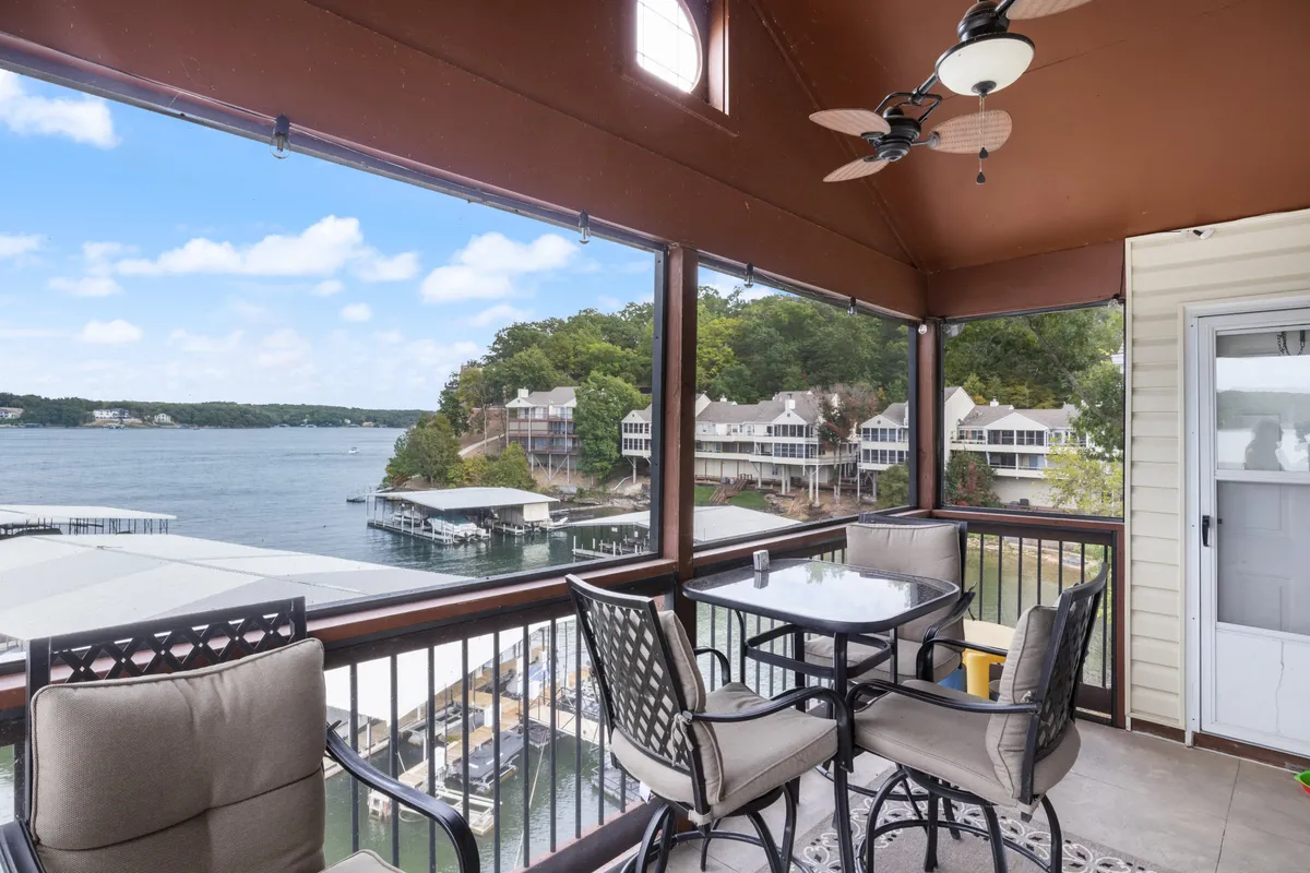 This exterior image presents a serene lakeside view with comfortable outdoor seating and a ceiling fan, all framed by lush greenery. The tranquil waters of the lake are visible in the background, suggesting a perfect spot for relaxation or romantic moments.