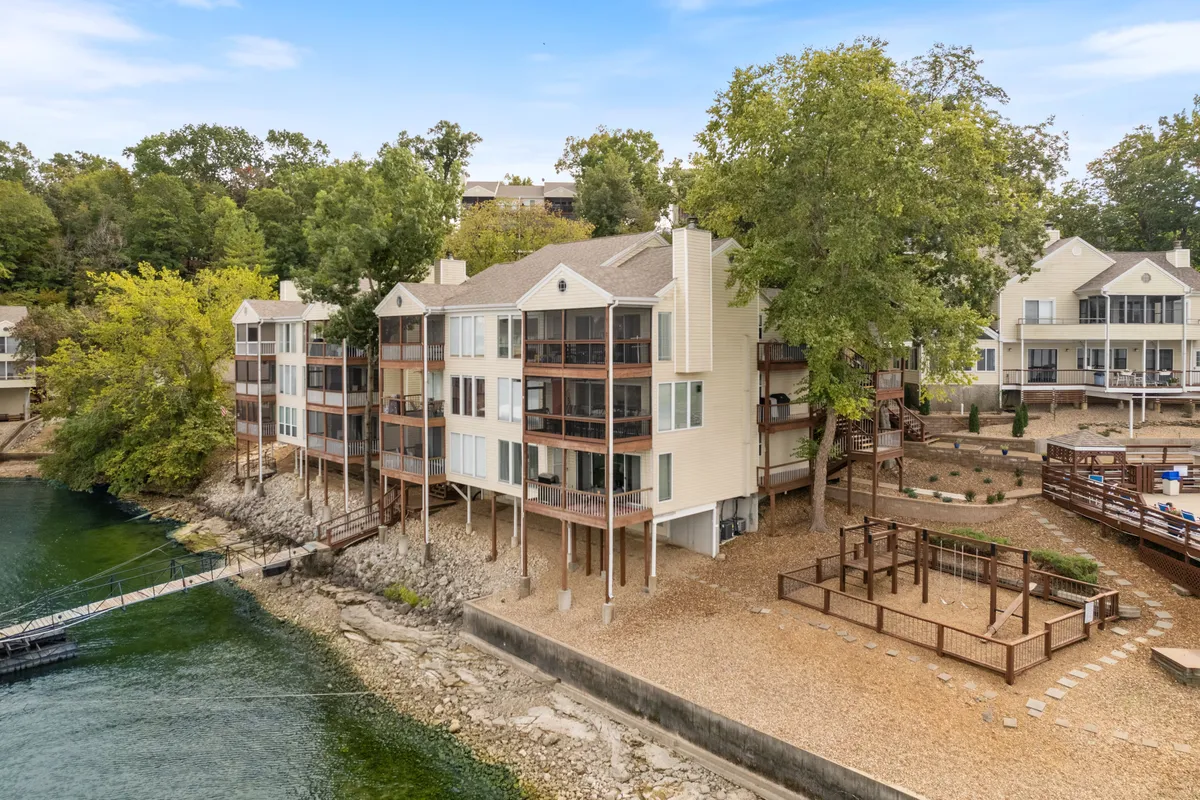 A panoramic exterior view of the lakeshore, with modern condo buildings, wooden decks, lush greenery, and the expansive lakefront. The communal decks and open green spaces are ideal for socializing, while the lake access hints at nearby dining, nightlife, and entertainment options.