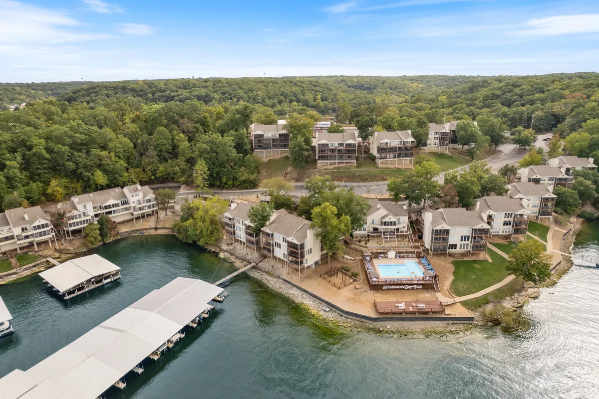 A wide exterior view capturing the resort's swimming pool overlooking the lake, marinas, wooded areas, and multiple residential buildings set along the water. The pool area is spacious, inviting for group fun and relaxation with plenty of seating and a clear connection to the water activities beyond.