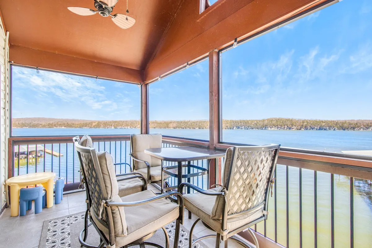 This image shows the screened-in lakefront balcony, complete with outdoor seating, a ceiling fan, and panoramic views of the water. The serene atmosphere invites morning coffees, reading, or unwinding with friends while soaking in the lake scenery and sunsets.