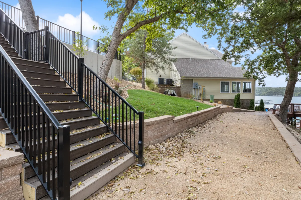 This exterior shot features a gentle staircase leading to a green lawn and the waterfront, with the house visible in the backdrop. The peaceful setting is ideal for walks, lakeside gatherings, or simply enjoying the changing seasons by the water.