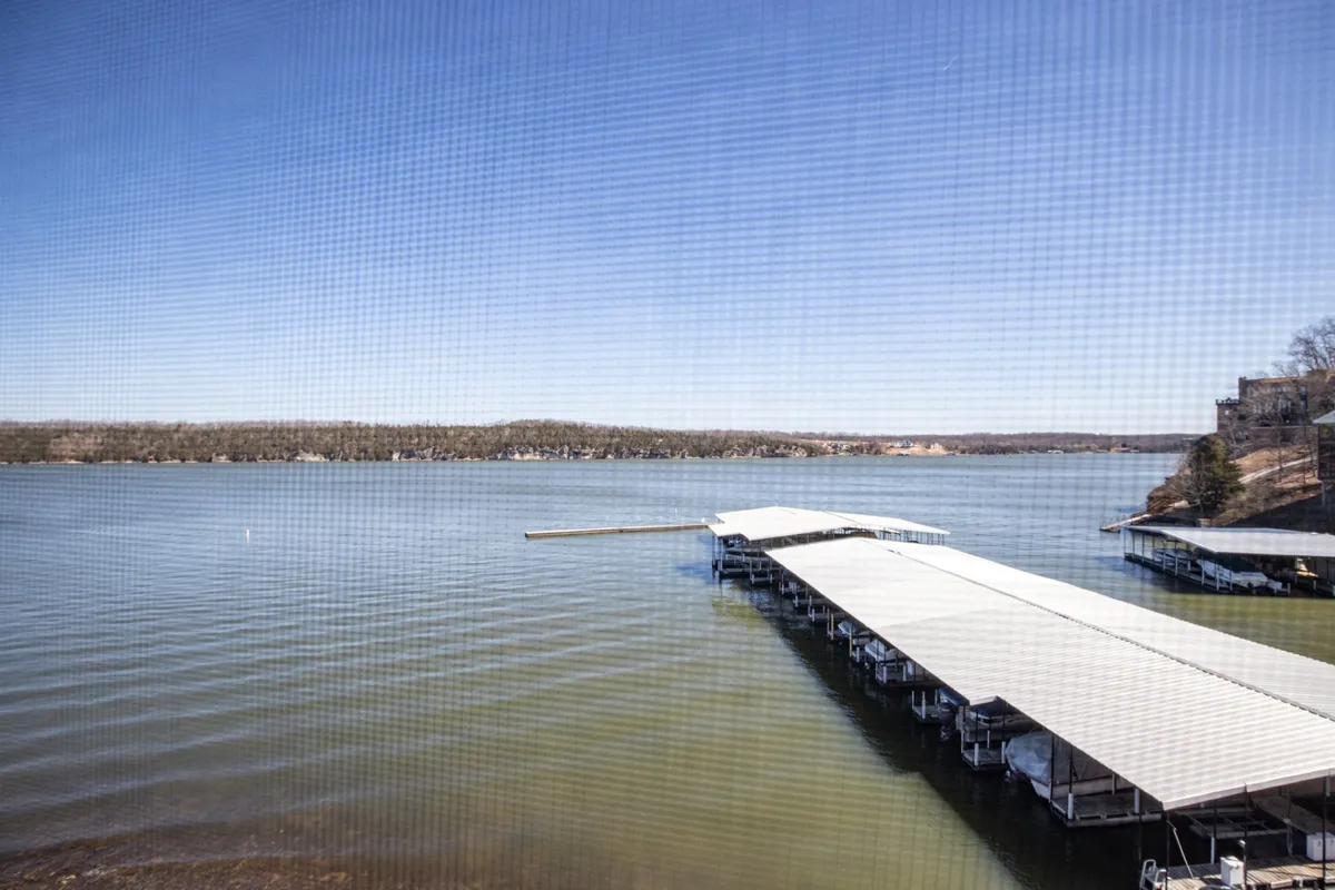 This image features a dock stretching out over the lake, with the tranquil water and a backdrop of trees meeting the horizon. The scene is calm and inviting, suggesting direct access to the lake for boating, fishing, or simply relaxing by the water's edge.