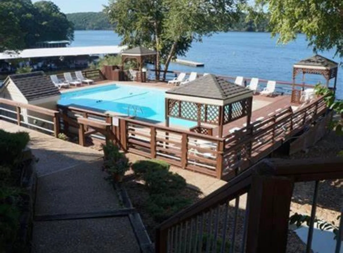 This image captures the inviting swimming pool with a surrounding sun deck, gazebos for shade, and a sweeping view of the lake beyond. Lounge chairs and open spaces make it ideal for sunbathing, swimming, or relaxing while watching lake activities.